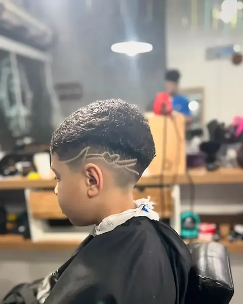 Criança na cadeira da barbearia com corte degradê e desenho lateral